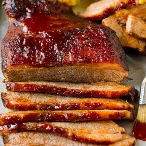 An oven baked beef brisket cut into slices and served alongside corn on the cob.