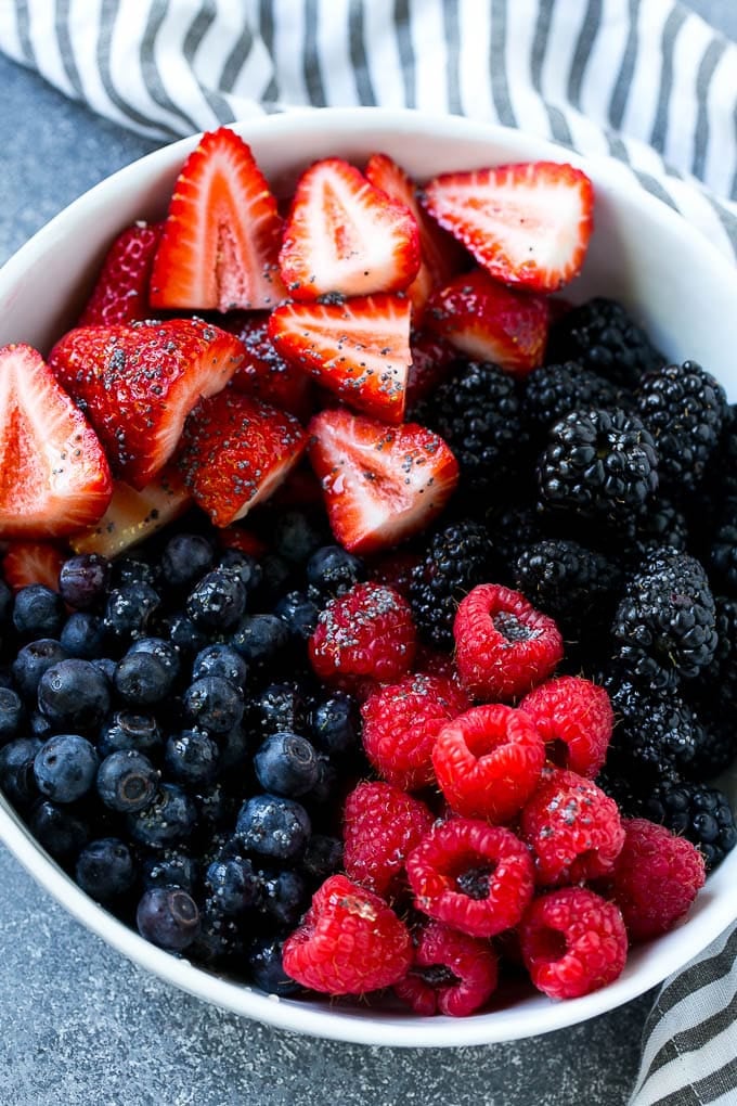 A bowl of blueberries, raspberries, blackberries and strawberries topped with poppy seed dressing.