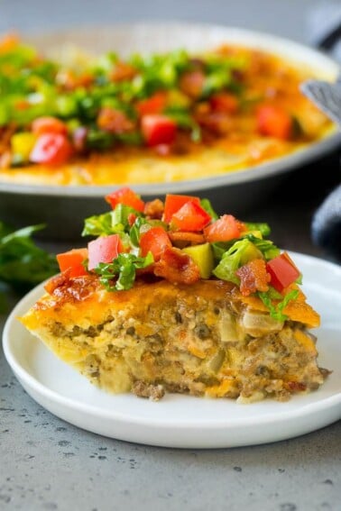 A slice of cheeseburger pie garnished with shredded lettuce, diced tomatoes and pickles.