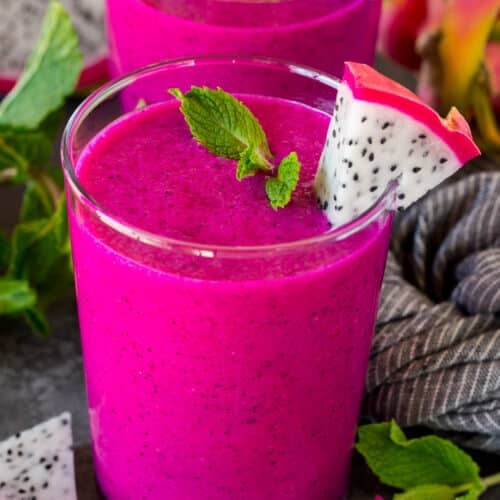Two cups of dragon fruit smoothie topped with mint and fresh dragon fruit.