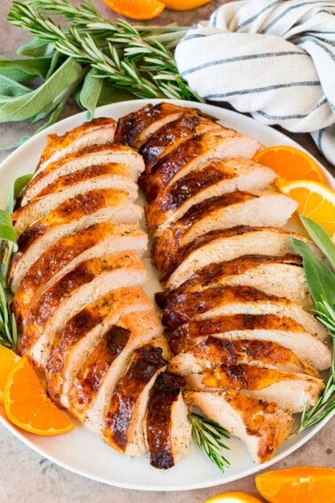 Sliced grilled turkey breast on a platter with herbs and citrus.