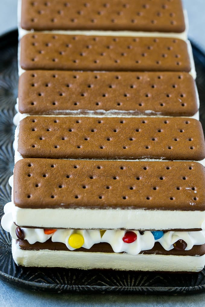 Layers of an ice cream sandwich cake with whipped topping and chocolate candy.