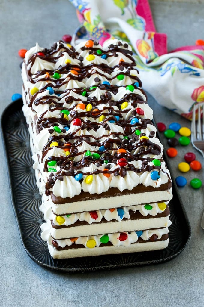 An ice cream sandwich cake decorated with whipped topping, hot fudge and chocolate candies.