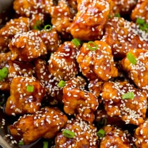 Crispy sesame chicken in a pan, coated in a sweet and savory sauce and sesame seeds.