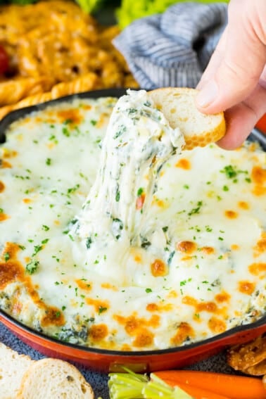 A slice of bread scooping up a serving of spinach artichoke dip.