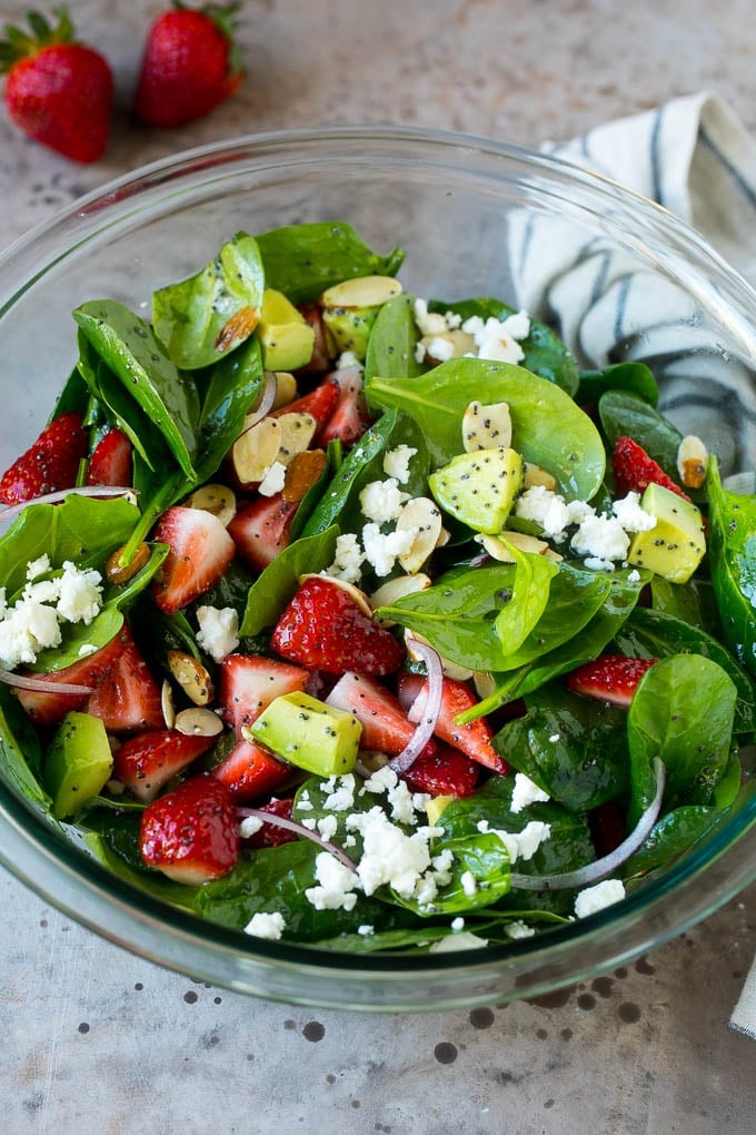 A bowl of strawberry spinach salad with feta cheese, almonds and avocado.
