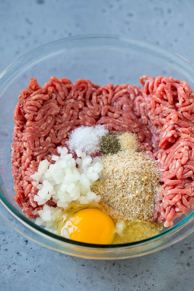 Ground beef, onion, breadcrumbs and seasonings in a bowl.